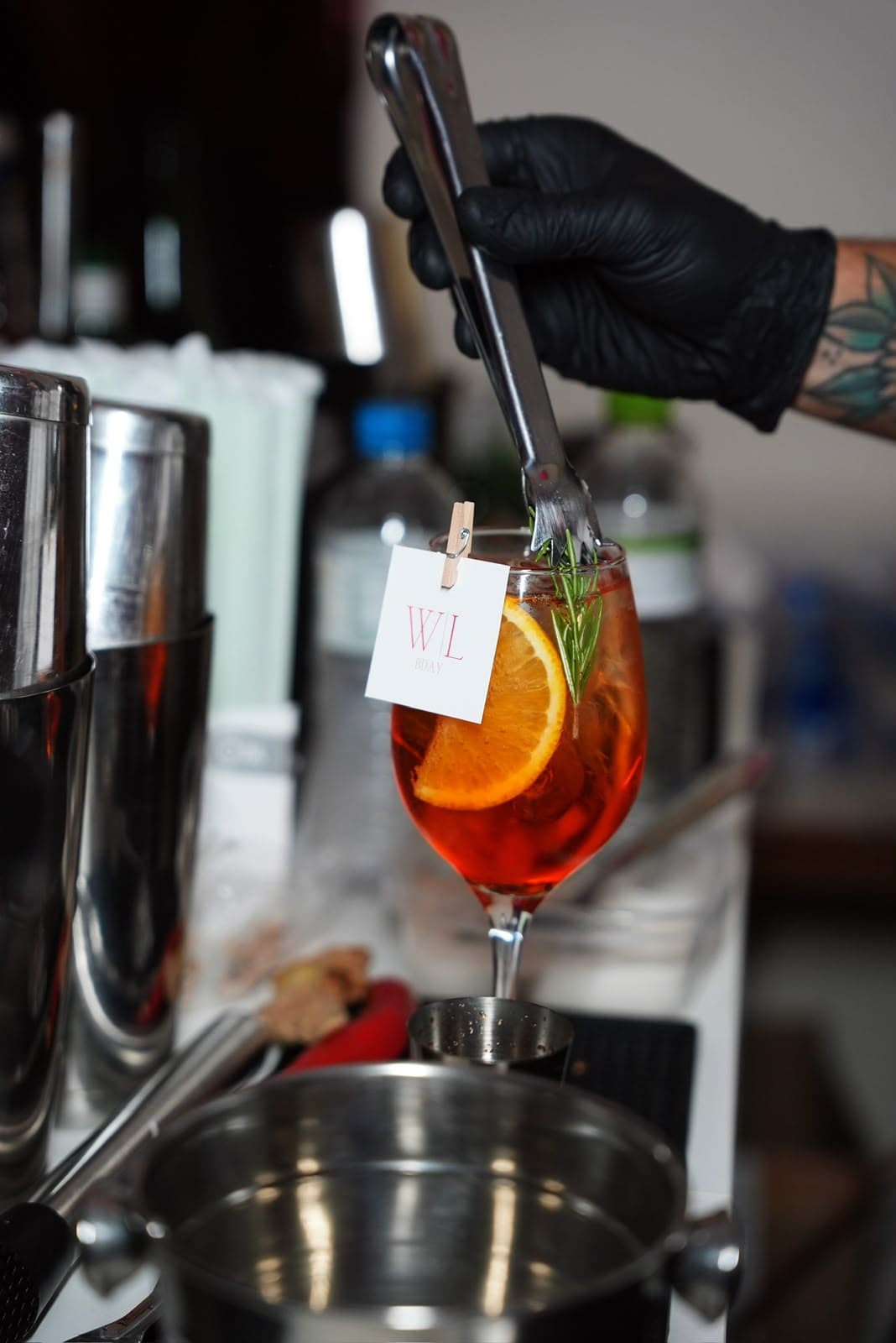 Mão de bartender finalizando um coquetel com laranja e ramo de alecrim